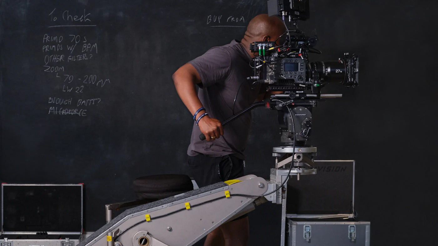 Person operating a large film camera with a chalkboard in the background